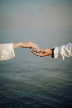 two people holding each other's hand over the ocean with water in the background