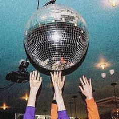 two people reaching for a disco ball in the air with their hands up to it