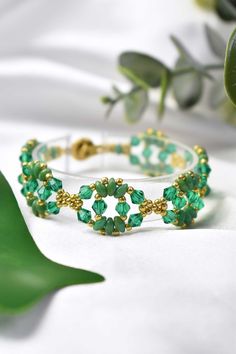 a close up of a bracelet with green beads and gold accents on a white surface