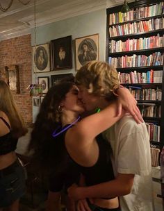 two people kissing each other in front of a bookshelf with many books on the shelves