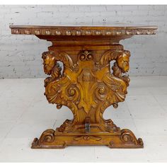 an old wooden table with carvings on the top and bottom, against a white brick wall