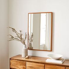 a white vase sitting on top of a wooden dresser next to a mirror and bowl