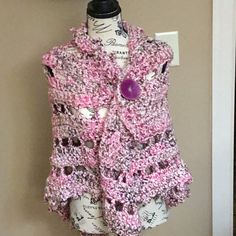 a crocheted vest hanging on a wall next to a coat hanger with buttons