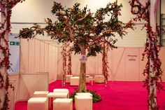 a room with pink carpet, white benches and a large tree in the center that has red flowers on it