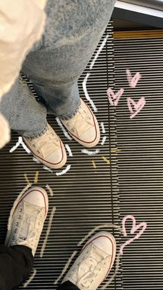 two people standing on an escalator with their feet in the air and hearts drawn on the floor