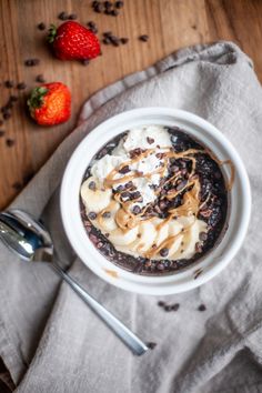 a bowl filled with chocolate pudding and whipped cream next to two strawberries on a wooden table