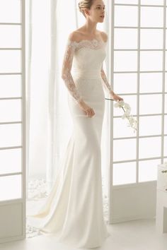 a woman in a white wedding dress is standing near a window and holding a bouquet