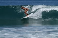 a woman riding a wave on top of a white surfboard in the middle of the ocean