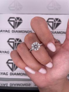 a woman's hand with a diamond ring on top of her finger and white nails