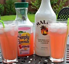 two bottles and three glasses filled with drinks on top of a metal table in front of a fence