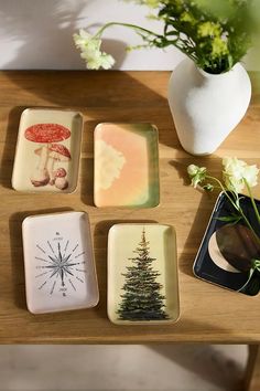 four small trays with designs on them sitting on a table next to a vase