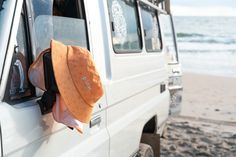 an orange hat is hanging out the window of a white truck at the beach with waves in the background