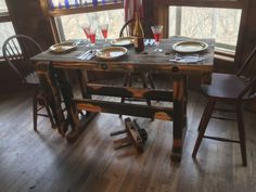 the table is set for two with plates and wine glasses on it in front of a window