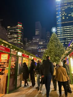 people are walking around in front of a christmas tree on the boardwalk at night time