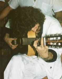 a man with long hair playing an acoustic guitar while sitting in a chair next to other people