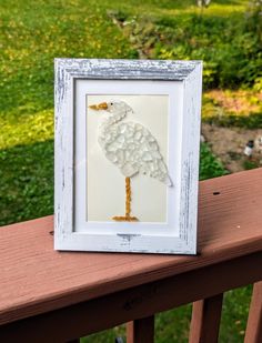 a white frame with a bird made out of paper on top of a wooden rail