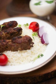 some meat and rice on a white plate with tomatoes, onions, and cherry tomatoes