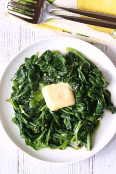 a white plate topped with spinach covered in butter on top of a wooden table