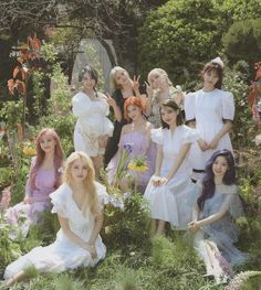 a group of women in white dresses sitting on the ground surrounded by flowers and plants