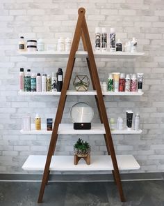 a white shelf with various items on it in front of a brick wall and wooden ladder