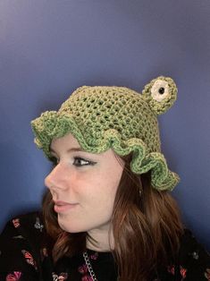 a woman wearing a green crocheted hat with an eye patch on the top