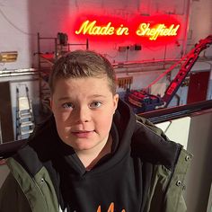 a young boy holding a hot dog in front of a neon sign that reads made in sheffield