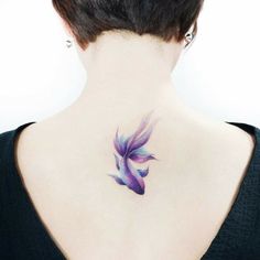 the back of a woman's neck with a purple and blue fish tattoo on it