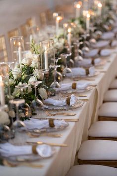 a long table is set with white flowers and candles for an elegant dinner or reception