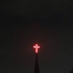 a red cross is lit up in the dark sky above a church steeple at night