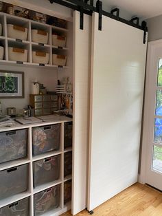 an open sliding door in a room with lots of bins on the floor and shelves