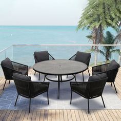 an outdoor table and chairs on a deck overlooking the ocean, with palm trees in the background