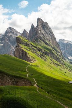 the mountains are covered in green grass and there is a path going through them that leads to a house