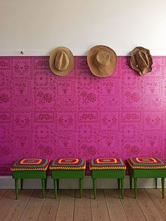 three green benches in front of a pink wall with two hats on the top of it