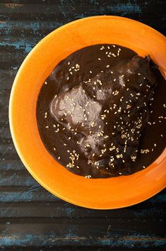 an orange bowl filled with chocolate pudding on top of a wooden table next to a cup of coffee