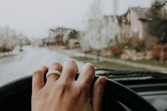 a person's hand on the steering wheel of a car, while it is raining