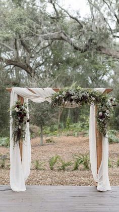 an outdoor wedding ceremony setup with white drapes and greenery on the altar, surrounded by trees