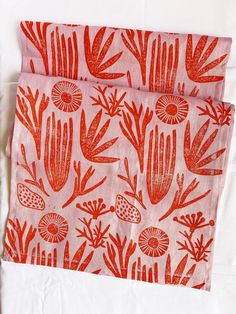 two napkins with red designs on them sitting on a white tablecloth next to each other