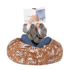 a person sitting on a bean bag chair reading a book while wearing a leopard print coat