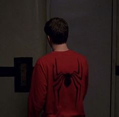 a young man in a red spider - man shirt is looking at the door to another room