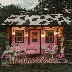 a small pink and black shed with white furniture on it's front lawn area