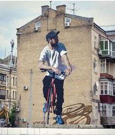 a man riding a bike in front of a building with a mural on it's side