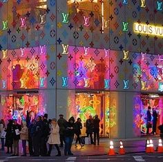 a group of people standing in front of a louis vuitton store at night