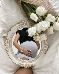 a pregnant woman laying on top of a bed next to a bouquet of white flowers