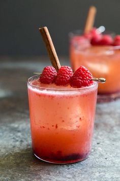 two glasses filled with raspberry punch on top of a stone counter next to cinnamon sticks