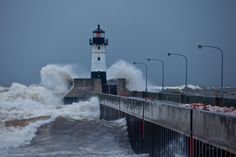 waves crash over the break wall and lighthouse at seawall in storm - ridden weather