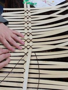 two hands on top of a wooden structure that is made out of strips of wood