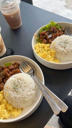 two plates with rice, meat and vegetables are on a table next to cups of coffee