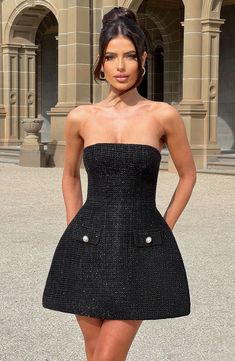 a woman standing in front of a building wearing a black dress with buttons on it