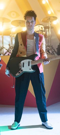 a man holding a guitar while standing in front of a stage with musical equipment on it