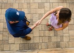 two people holding hands while standing on a brick floor next to each other, looking down at the ground